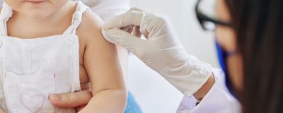 Doctor in rubber gloves wiping injection site on arm of little girl before vaccination