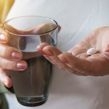 Woman holding a glass of water in one hand and pill in the other