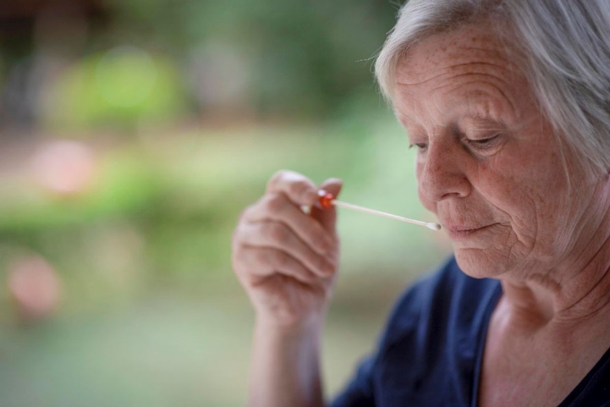 Woman with gray hair and navy shirt smelling a medical swab.