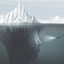 Surreal illustration of the mind, represented by a person-shaped iceberg. A scuba diver illuminates the dark side of the iceberg underwater with a flashlight.